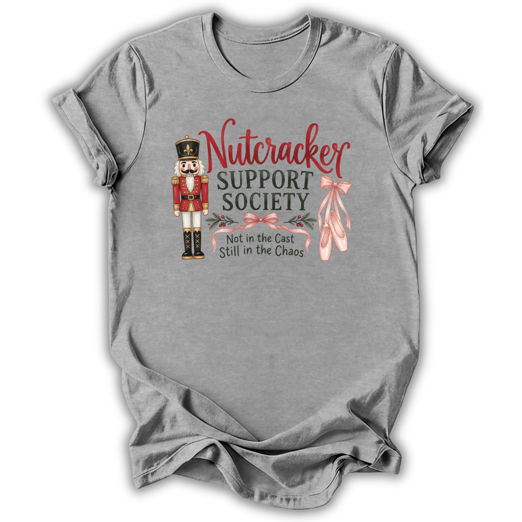 A heather gray short-sleeve t-shirt with a graphic on the front featuring a nutcracker, pink ballet slippers, and the text 'Nutcracker Support Society Not in the Cast Still in the Chaos'.