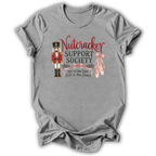 A heather gray short-sleeve t-shirt with a graphic on the front featuring a nutcracker, pink ballet slippers, and the text 'Nutcracker Support Society Not in the Cast Still in the Chaos'.
