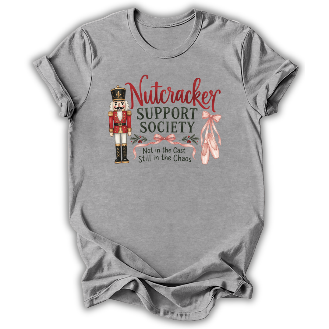 A heather gray short-sleeve t-shirt with a graphic on the front featuring a nutcracker, pink ballet slippers, and the text 'Nutcracker Support Society Not in the Cast Still in the Chaos'.