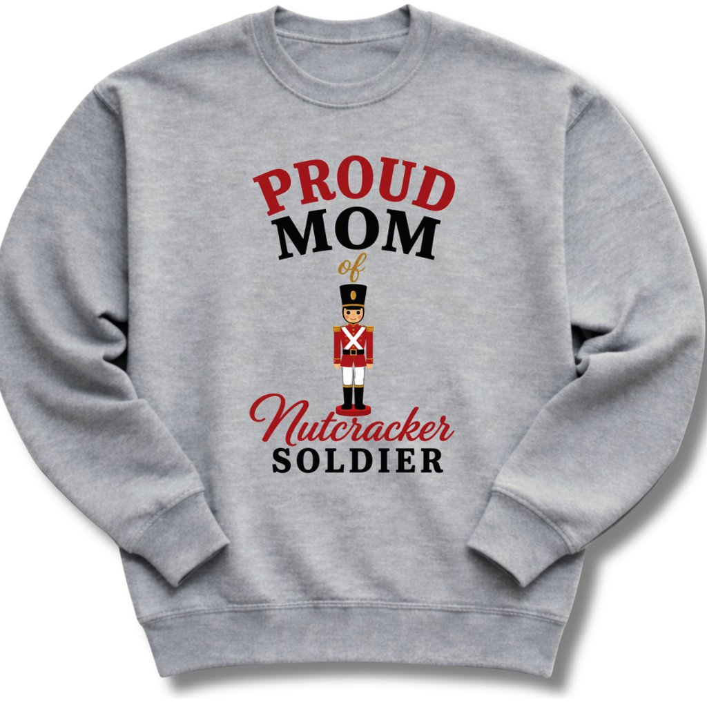 A heather gray crewneck sweatshirt featuring a graphic print that reads 'PROUD MOM of Nutcracker SOLDIER' in red and black lettering, with a small nutcracker soldier illustration in the center.