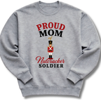 A heather gray crewneck sweatshirt featuring a graphic print that reads 'PROUD MOM of Nutcracker SOLDIER' in red and black lettering, with a small nutcracker soldier illustration in the center.