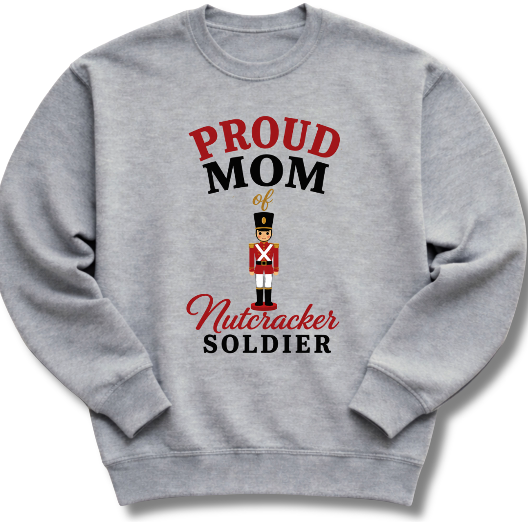 A heather gray crewneck sweatshirt featuring a graphic print that reads 'PROUD MOM of Nutcracker SOLDIER' in red and black lettering, with a small nutcracker soldier illustration in the center.