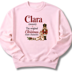 A light pink crewneck sweatshirt featuring a custom holiday graphic with the text 'Clara (noun): The original Christmas main character.' and an illustration of a nutcracker and ballet shoes.