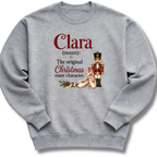 A heather gray crewneck sweatshirt featuring a custom dictionary-style graphic of the word 'Clara' with a nutcracker and holiday-themed illustration.