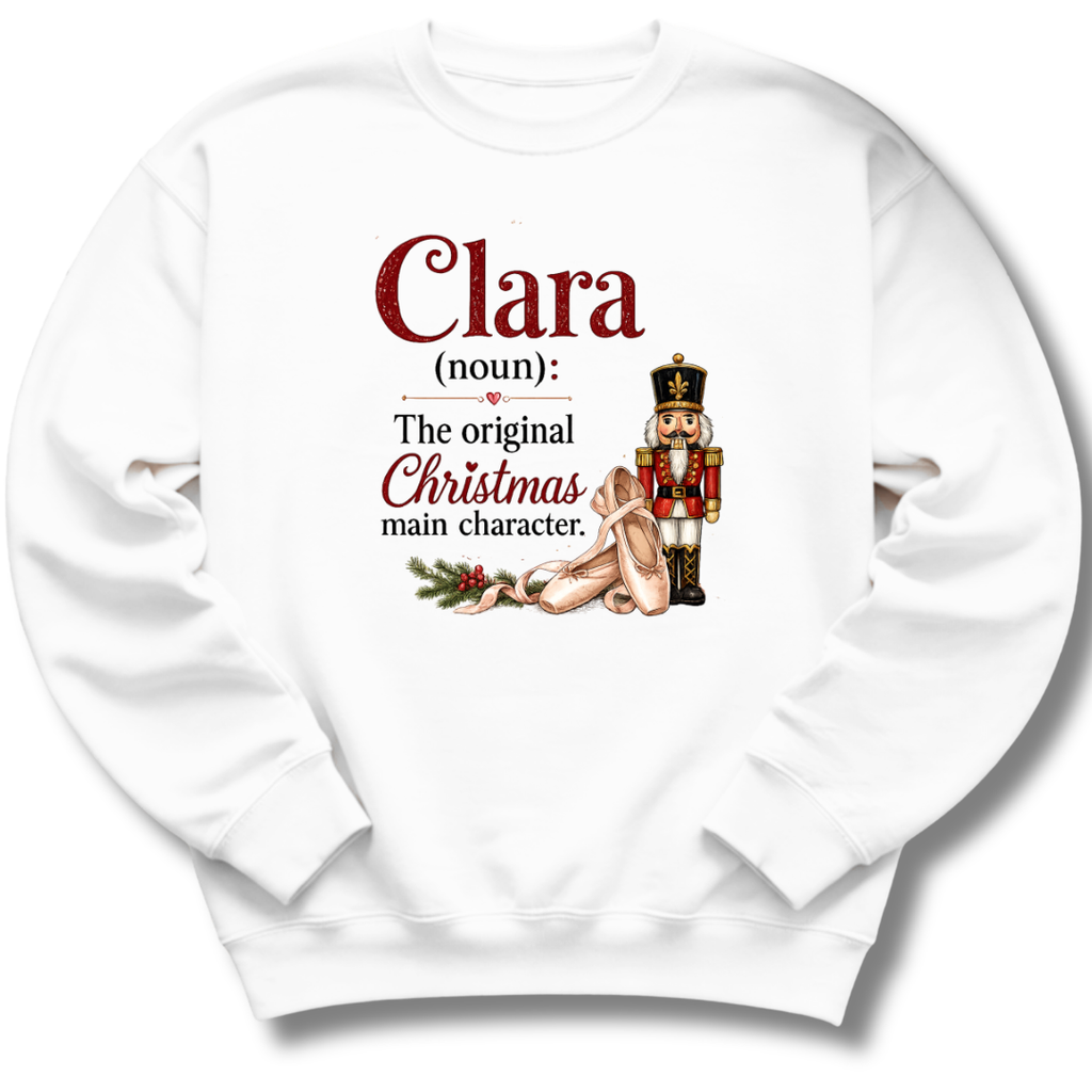 A white crewneck sweatshirt with a custom holiday graphic on the front. The graphic features the text 'Clara (noun): The original Christmas main character.
