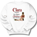 A white crewneck sweatshirt with a custom holiday graphic on the front. The graphic features the text 'Clara (noun): The original Christmas main character.