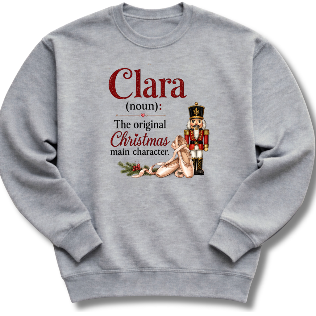 A heather gray crewneck sweatshirt featuring a custom dictionary-style graphic of the word 'Clara' with a nutcracker and holiday-themed illustration.