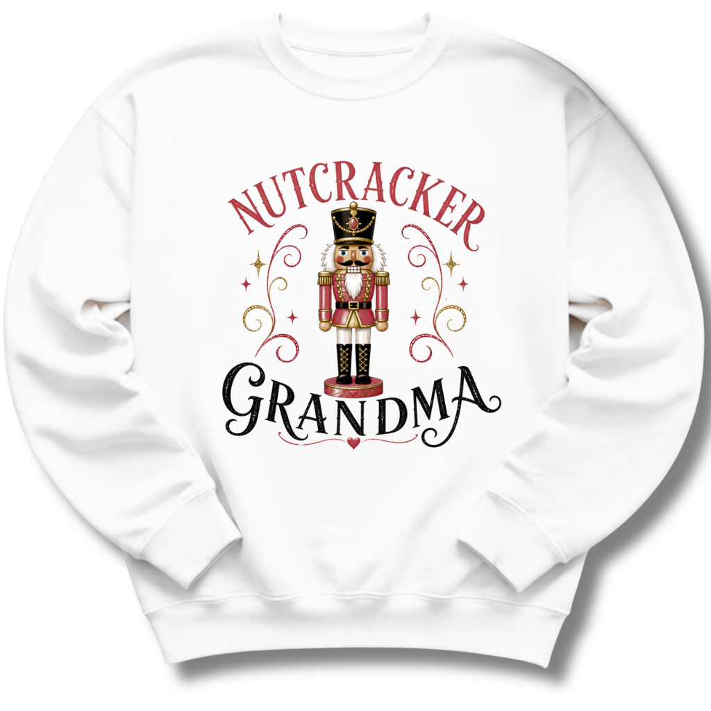 A white crewneck sweatshirt featuring a graphic print of a nutcracker soldier with the words 'NUTCRACKER GRANDMA' in red and black lettering, surrounded by decorative gold swirls and stars.