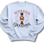 A light blue crewneck sweatshirt featuring a festive graphic print of a nutcracker soldier with the words 'NUTCRACKER GRANDMA' in red and black lettering.
