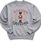 A heather gray crewneck sweatshirt featuring a festive graphic of a nutcracker soldier with the words 'NUTCRACKER GRANDMA' in red and black script.