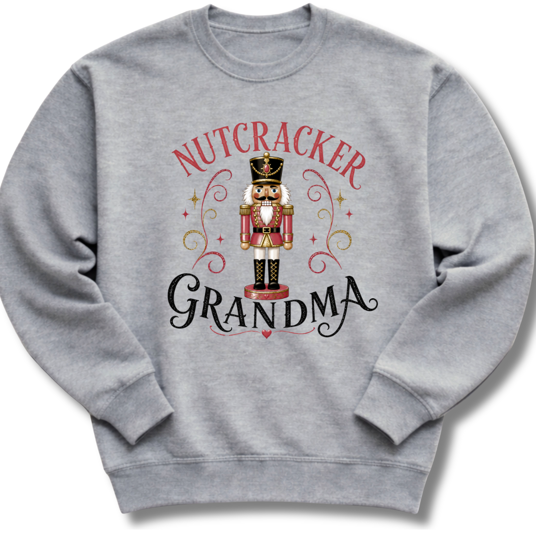 A heather gray crewneck sweatshirt featuring a festive graphic of a nutcracker soldier with the words 'NUTCRACKER GRANDMA' in red and black script.