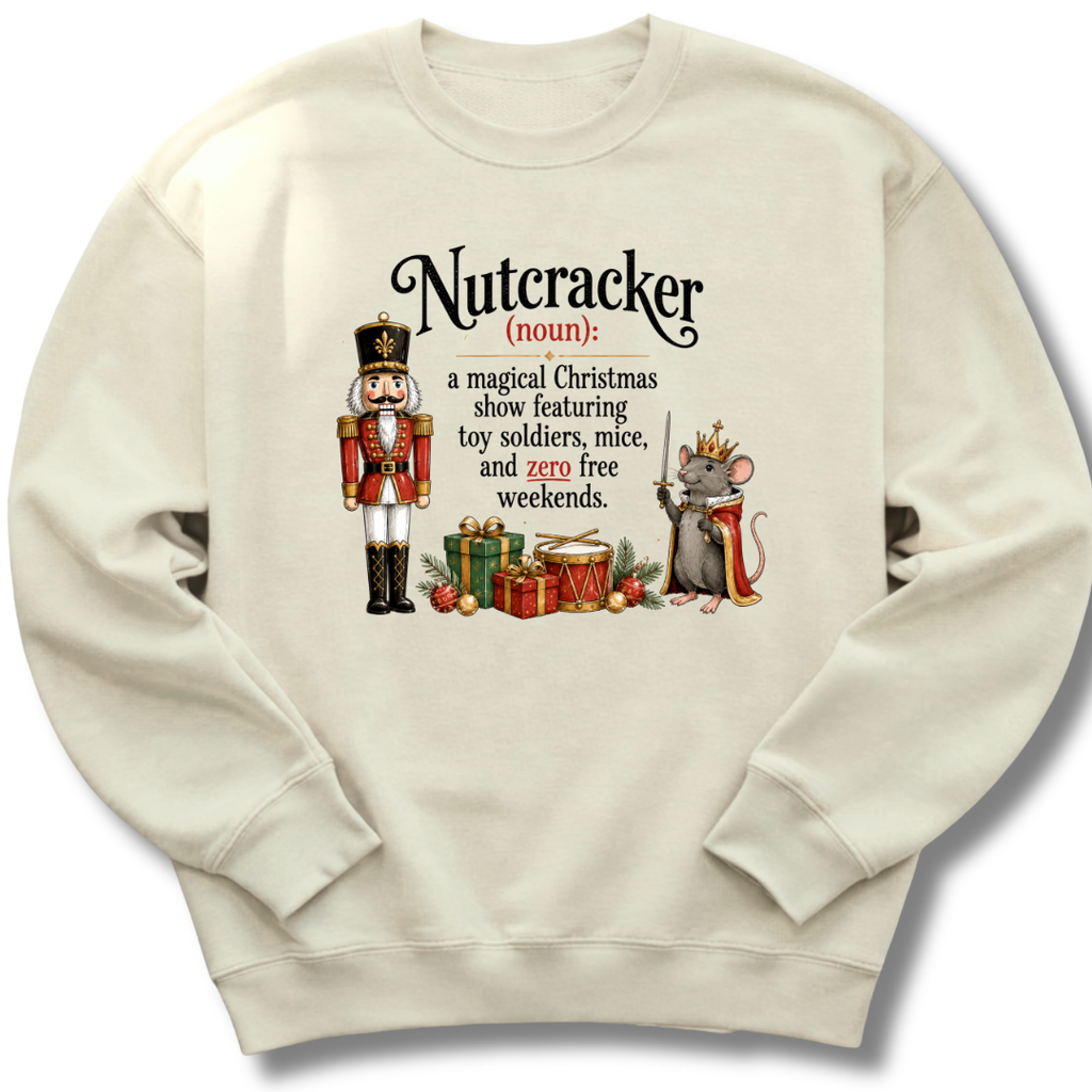 A cream-colored crewneck sweatshirt featuring a humorous dictionary-style definition of 'Nutcracker' printed on the front, complete with an illustration of a nutcracker soldier and a mouse with a crown.