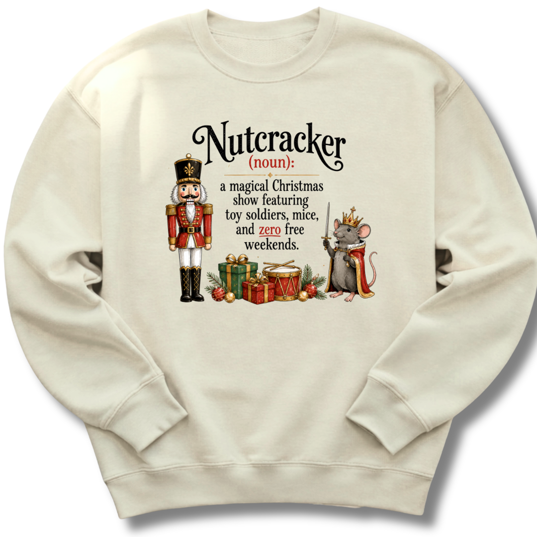 A cream-colored crewneck sweatshirt featuring a humorous dictionary-style definition of 'Nutcracker' printed on the front, complete with an illustration of a nutcracker soldier and a mouse with a crown.