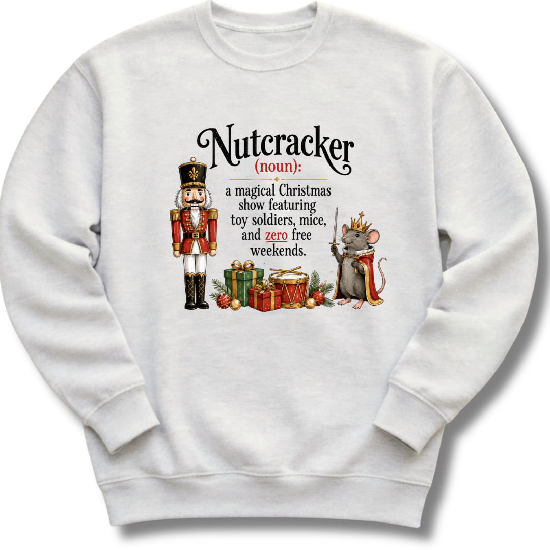 A white crewneck sweatshirt featuring a printed graphic of a nutcracker and a mouse with a dictionary-style definition of 'Nutcracker' under the word 'noun'.