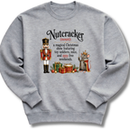 A heather gray crewneck sweatshirt featuring a humorous Christmas-themed graphic of a nutcracker and a mouse with a crown, accompanied by a printed definition of 'Nutcracker'.