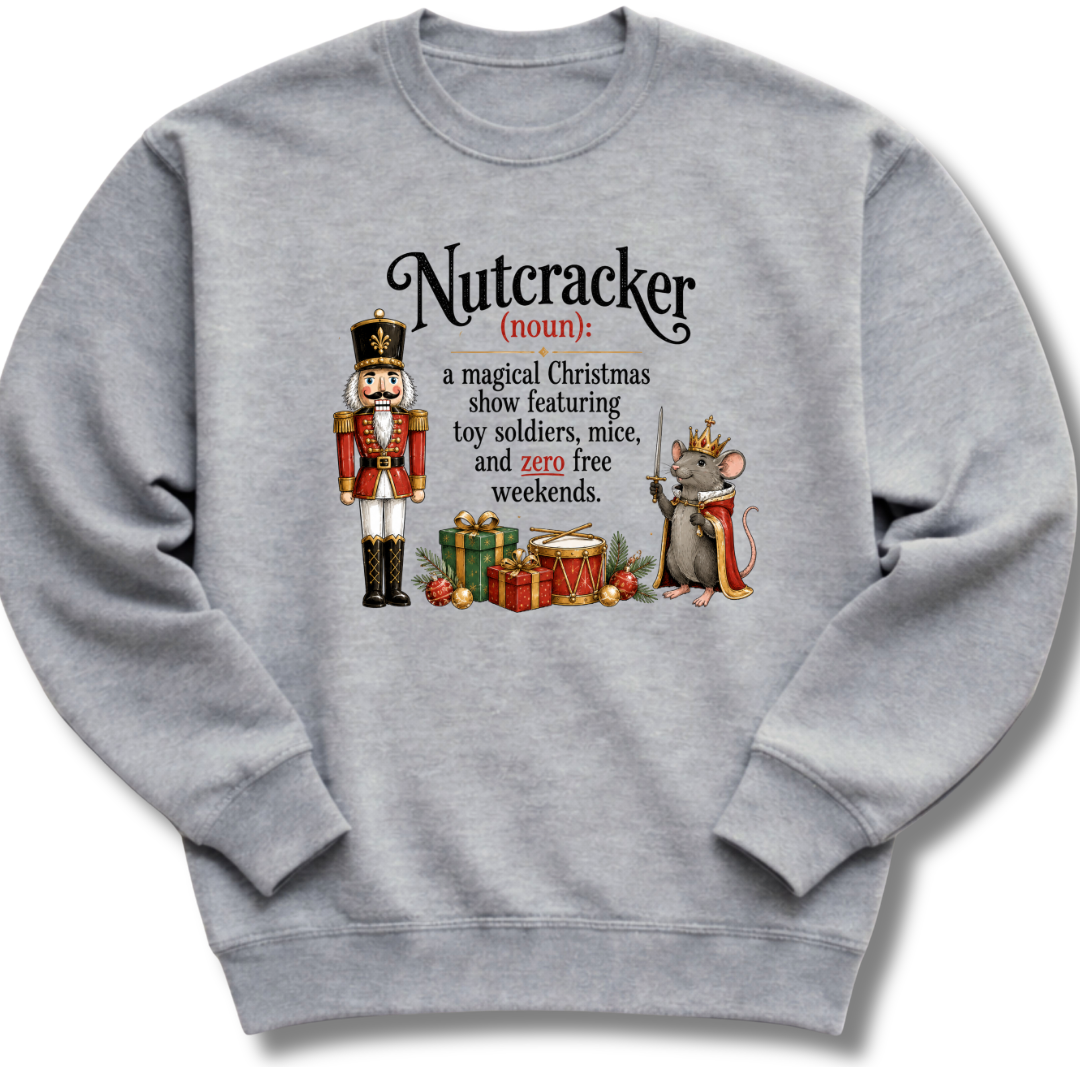 A heather gray crewneck sweatshirt featuring a humorous Christmas-themed graphic of a nutcracker and a mouse with a crown, accompanied by a printed definition of 'Nutcracker'.