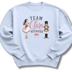 A light blue crewneck sweatshirt featuring a graphic print of a ballerina in a pink dress, a nutcracker, and the text 'TEAM Clara NUTCRACKER' with a pink bow.