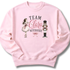 A light pink crewneck sweatshirt featuring a graphic print of a ballerina and a nutcracker with the text 'TEAM Clara NUTCRACKER' and a pink bow.