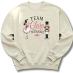 A cream-colored crewneck sweatshirt featuring a graphic print of a girl in a pink dress, a nutcracker, and the text 'TEAM Clara NUTCRACKER' with a pink bow.