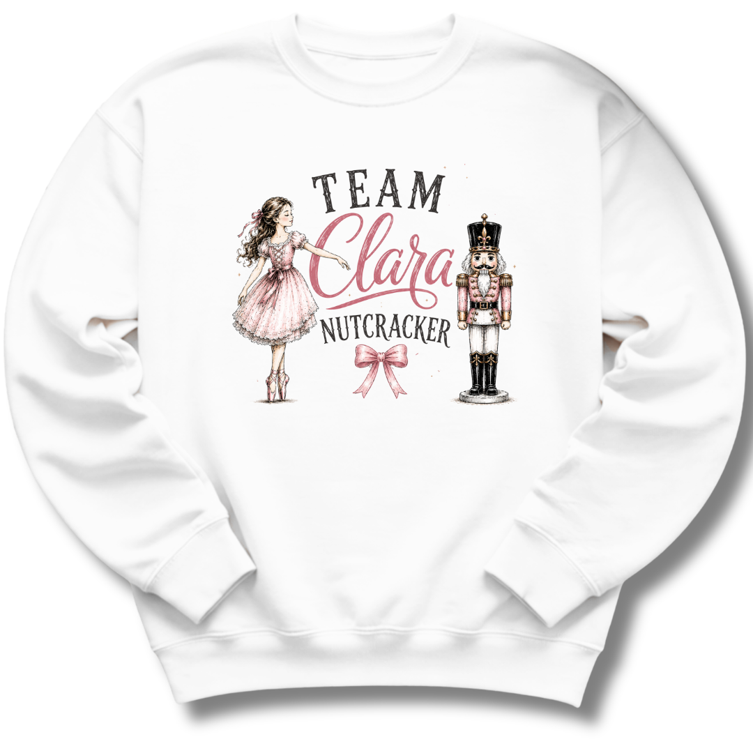 A white crewneck sweatshirt featuring a custom graphic print that reads 'TEAM Clara NUTCRACKER' in black and pink lettering, accompanied by illustrations of a girl in a pink dress and a nutcracker, set against a plain white background.