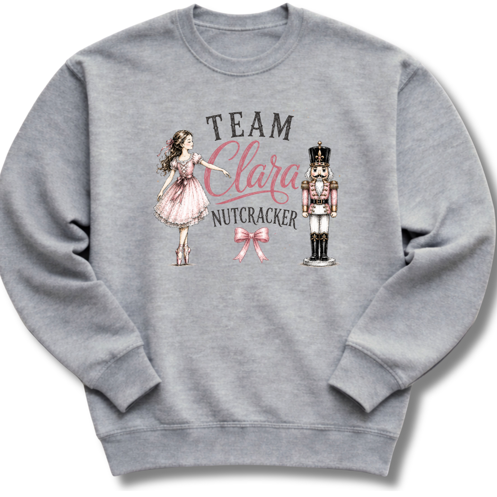 A heather gray crewneck sweatshirt featuring a graphic print of a girl in a pink dress, a nutcracker, and the text 'TEAM Clara NUTCRACKER' with a pink bow.