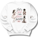A white crewneck sweatshirt featuring a whimsical graphic print of a girl in a pink dress, a nutcracker, a cat, and the text 'Just a Girl Who Loves Nutcracker' in black and pink script.
