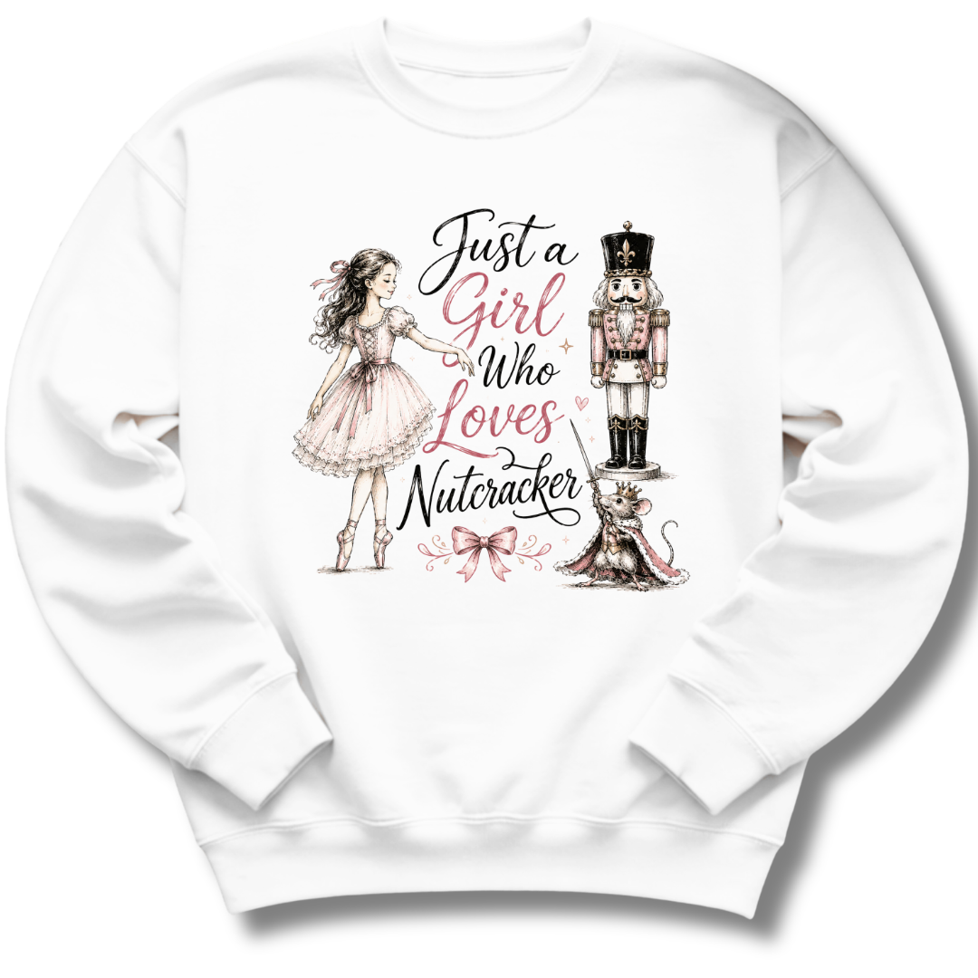 A white crewneck sweatshirt featuring a whimsical graphic print of a girl in a pink dress, a nutcracker, a cat, and the text 'Just a Girl Who Loves Nutcracker' in black and pink script.