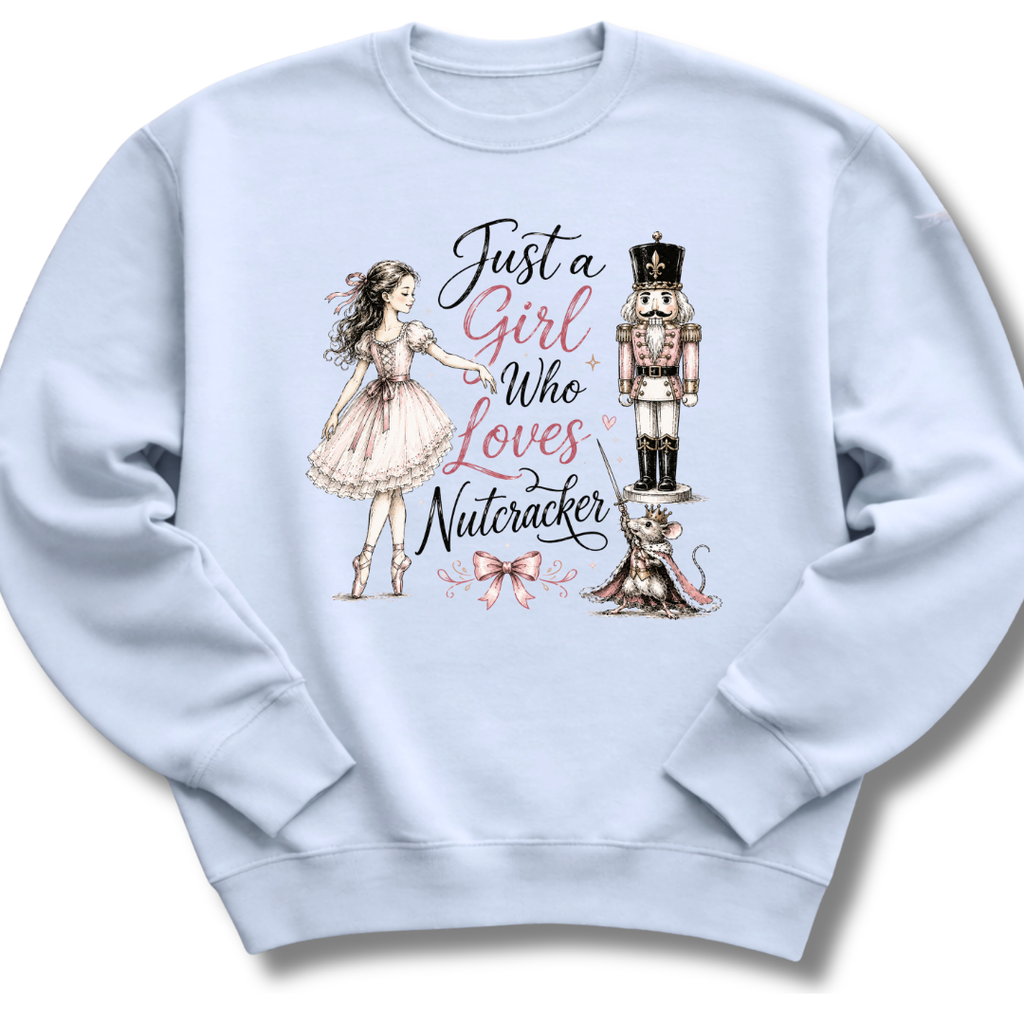 A light blue crewneck sweatshirt featuring a graphic print of a ballerina, a nutcracker, a cat, and the text 'Just a Girl Who Loves Nutcracker' in black and pink lettering.