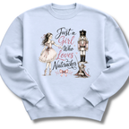 A light blue crewneck sweatshirt featuring a graphic print of a ballerina, a nutcracker, a cat, and the text 'Just a Girl Who Loves Nutcracker' in black and pink lettering.