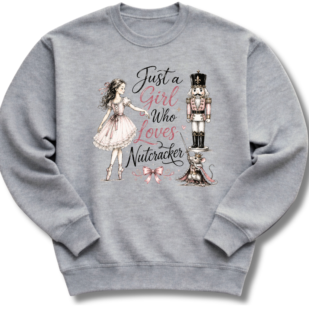 A heather gray crewneck sweatshirt featuring a graphic print of a ballerina in a pink dress, a nutcracker, a cat, and the text 'Just a Girl Who Loves Nutcracker' in pink and black script.