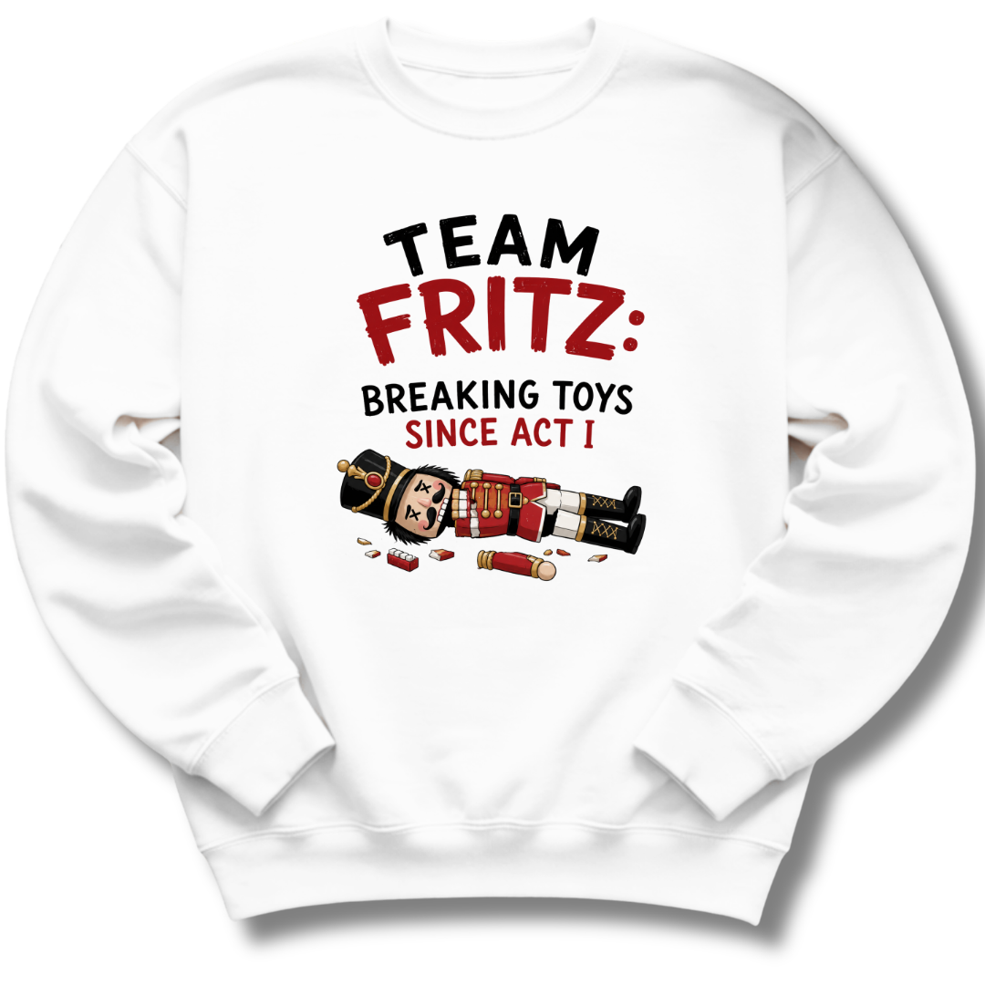 A white crewneck sweatshirt featuring a graphic print on the front with the text 'TEAM FRITZ: BREAKING TOYS SINCE ACT I' and an illustration of a broken nutcracker and toy pieces.