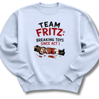 A light blue crewneck sweatshirt featuring a graphic print on the front with the text 'TEAM FRITZ: BREAKING TOYS SINCE ACT I' and an illustration of a broken nutcracker and toy pieces.