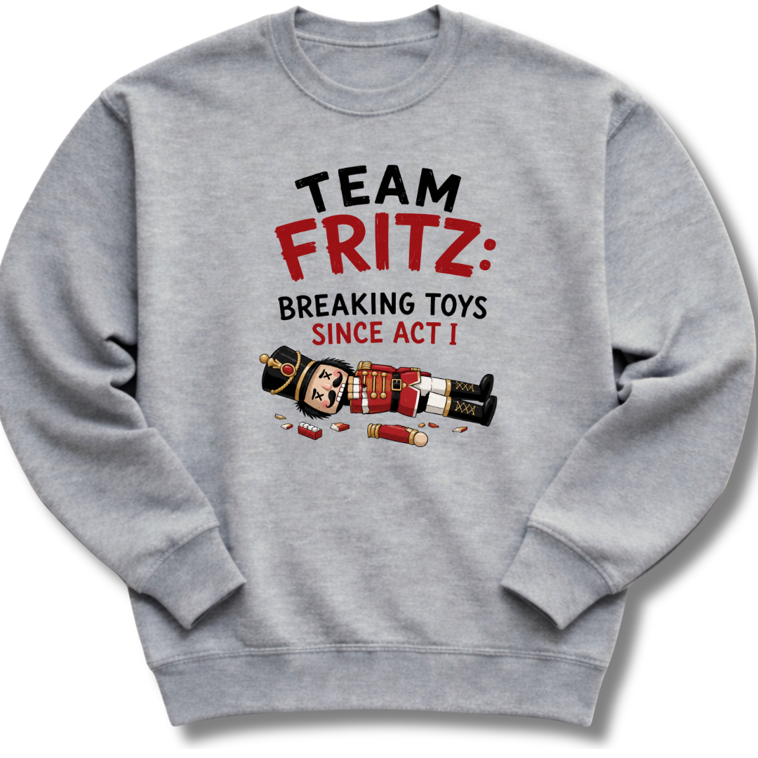 A heather gray crewneck sweatshirt featuring a graphic print on the front with the text 'TEAM FRITZ: BREAKING TOYS SINCE ACT I' and a cartoon illustration of a broken nutcracker and toy pieces.