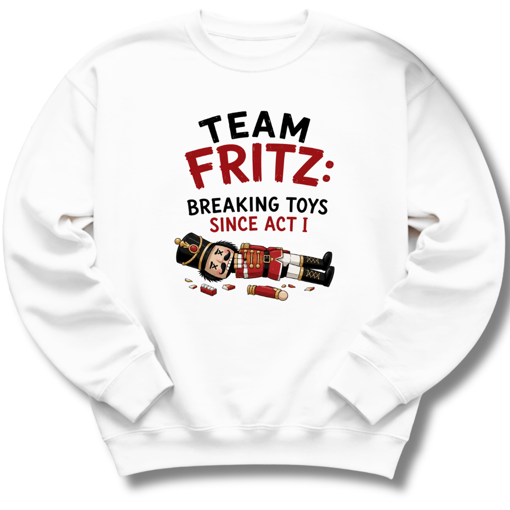 A white crewneck sweatshirt featuring a graphic print on the front with the text 'TEAM FRITZ: BREAKING TOYS SINCE ACT I' and an illustration of a broken nutcracker and toy pieces.