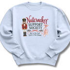 A light blue crewneck sweatshirt featuring a graphic print of a nutcracker, pink ballet slippers, and the text 'Nutcracker Support Society Not in the Cast Still in the Chaos'.