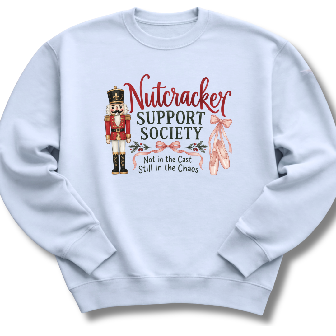 A light blue crewneck sweatshirt featuring a graphic print of a nutcracker, pink ballet slippers, and the text 'Nutcracker Support Society Not in the Cast Still in the Chaos'.