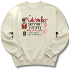 A cream-colored crewneck sweatshirt featuring a graphic design on the front. The design includes a nutcracker soldier, pink ballet slippers, and the text 'Nutcracker Support Society' and 'Not in the Cast Still in the Chaos'.