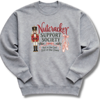A heather gray crewneck sweatshirt featuring a Nutcracker-themed graphic with the text 'Nutcracker Support Society' and 'Not in the Cast Still in the Chaos' alongside a nutcracker figure, pink bows, and ballet slippers.