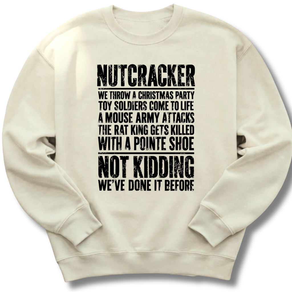 An off-white crewneck sweatshirt with black distressed text on the front that reads 'NUTCRACKER WE THROW A CHRISTMAS PARTY TOY SOLDIERS COME TO LIFE A MOUSE ARMY ATTACKS THE RAT KING GETS KILLED WITH A POINTE SHOE NOT KIDDING WE'VE DONE IT BEFORE.'.