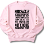 A light pink crewneck sweatshirt with a black distressed text graphic on the front that reads 'NUTCRACKER' followed by a humorous Christmas-themed story and 'NOT KIDDING WE'VE DONE IT BEFORE.'.