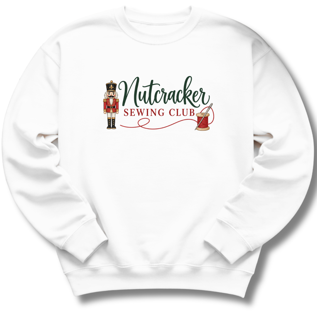A white crewneck sweatshirt featuring a graphic print on the chest that reads 'Nutcracker Sewing Club' in green and red lettering, accompanied by an illustration of a nutcracker and a spool of thread.