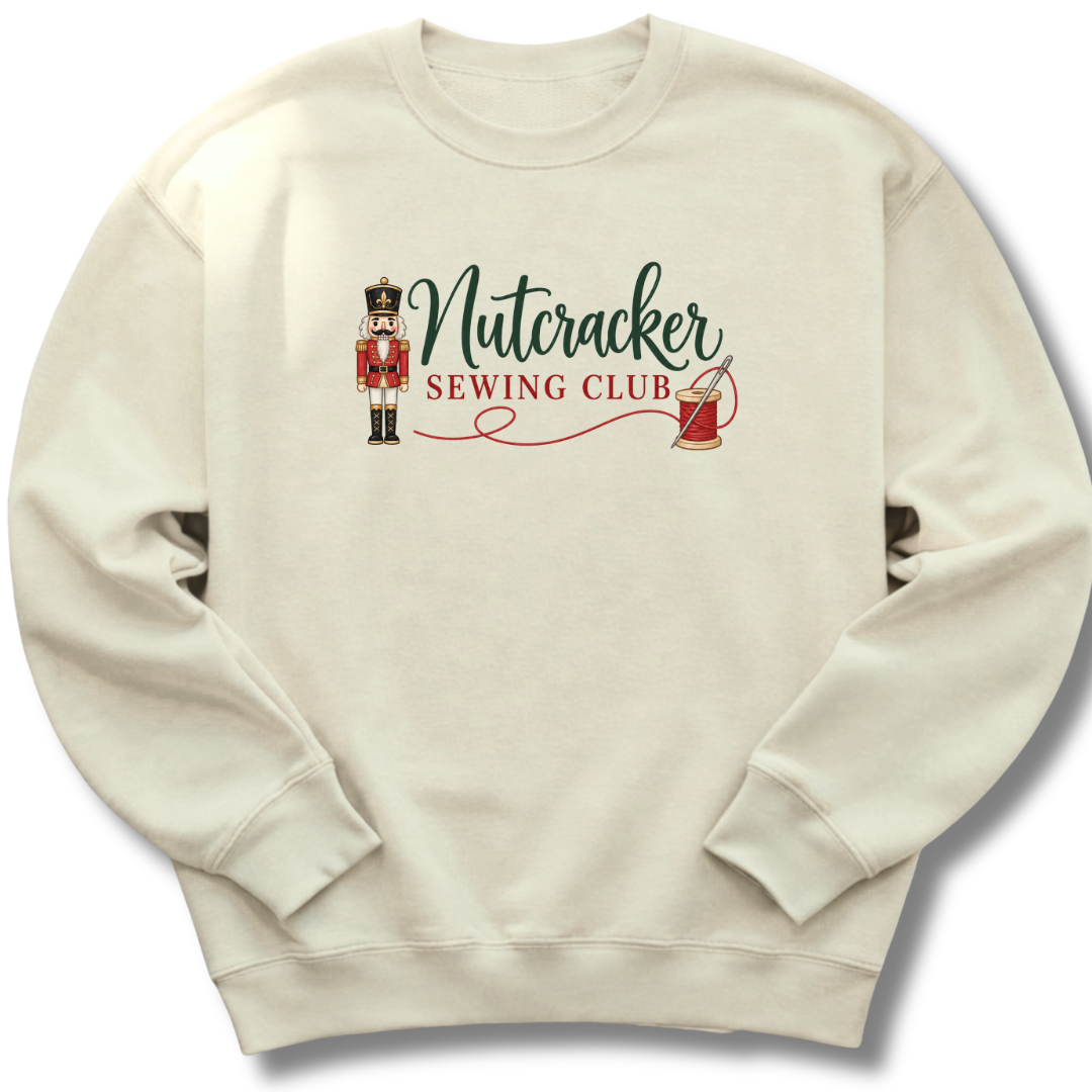 An off-white crewneck sweatshirt featuring a 'Nutcracker Sewing Club' graphic on the chest with a nutcracker figure, green script text, and red text.