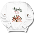 A white crewneck sweatshirt featuring a festive graphic print with the text 'Nutcracker Social Club' and an illustration of a nutcracker, pink ballet slippers, pine branches, and ornaments.