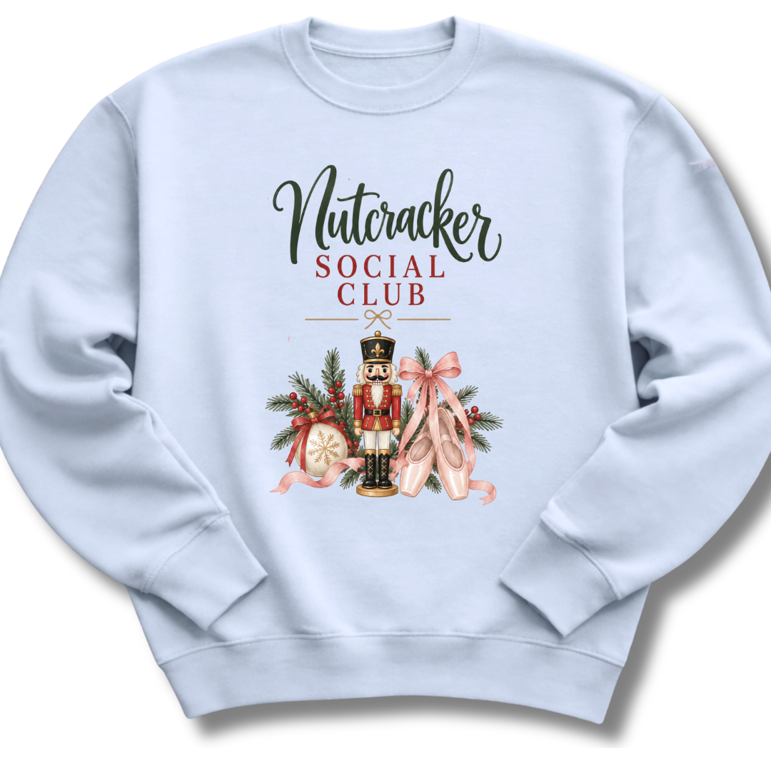 A light blue crewneck sweatshirt featuring a 'Nutcracker Social Club' graphic on the chest with a nutcracker, pink ballet slippers, and holiday decorations.