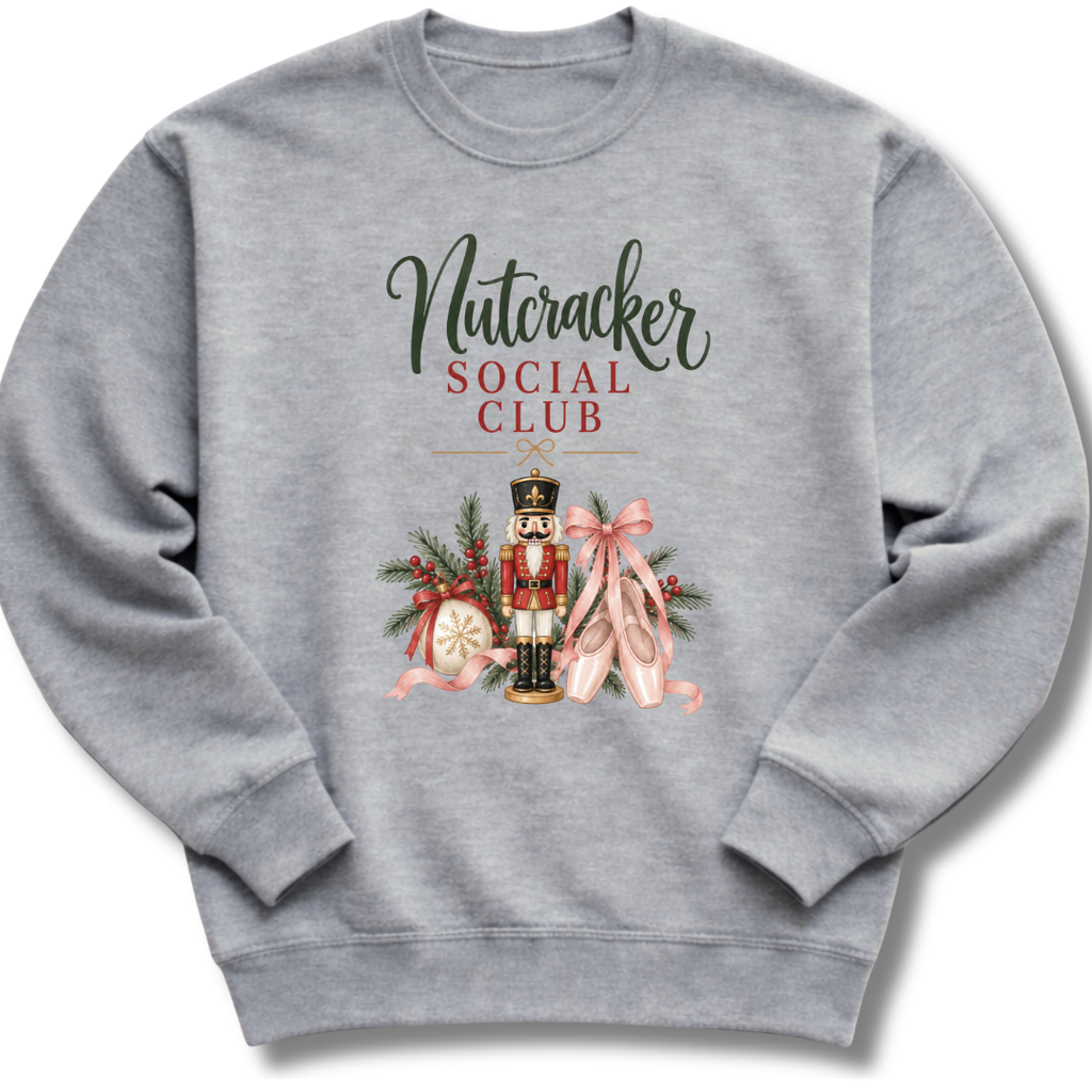 A heather gray crewneck sweatshirt featuring a festive graphic print on the front with the text 'Nutcracker Social Club' and an illustration of a nutcracker, pink ballet slippers, and holiday greenery.