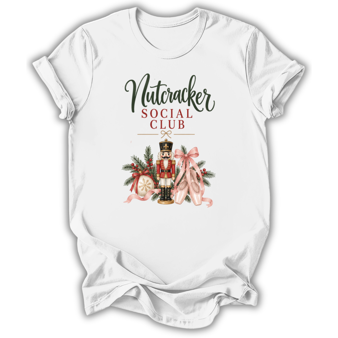 A white short-sleeve crewneck t-shirt with a graphic print on the front. The graphic features the text 'Nutcracker SOCIAL CLUB' in black and red lettering above an illustration of a nutcracker soldier decorated with a pink bow, green pine branches, and a gold hat.