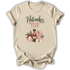 A beige short-sleeve t-shirt with a 'Nutcracker Social Club' graphic on the front, featuring a nutcracker, pink ribbons, and holiday greenery, displayed on a white background.