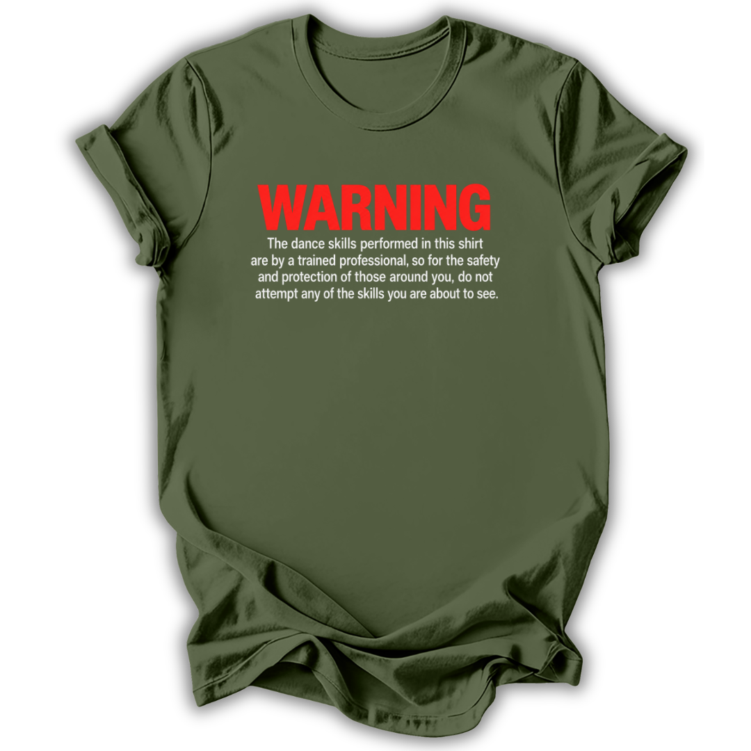 An olive green short-sleeve t-shirt with a humorous warning printed on the chest. The text reads 'WARNING' in bold red letters, followed by white text explaining that the dance skills shown are performed by a trained professional for safety and protection, advising against attempting those skills.