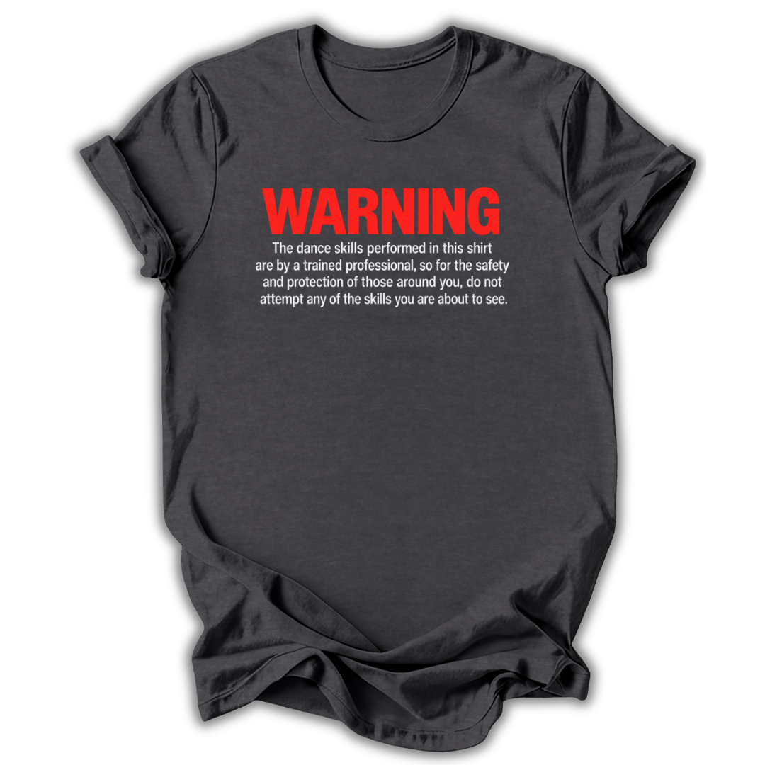 A dark gray crewneck t-shirt with a humorous safety warning printed on the chest. The text reads 'WARNING' in bold red letters, followed by smaller white text explaining that the dance skills shown in the shirt are performed by a trained professional for safety.