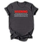 A dark gray crewneck t-shirt with a humorous safety warning printed on the chest. The text reads 'WARNING' in bold red letters, followed by smaller white text explaining that the dance skills shown in the shirt are performed by a trained professional for safety.